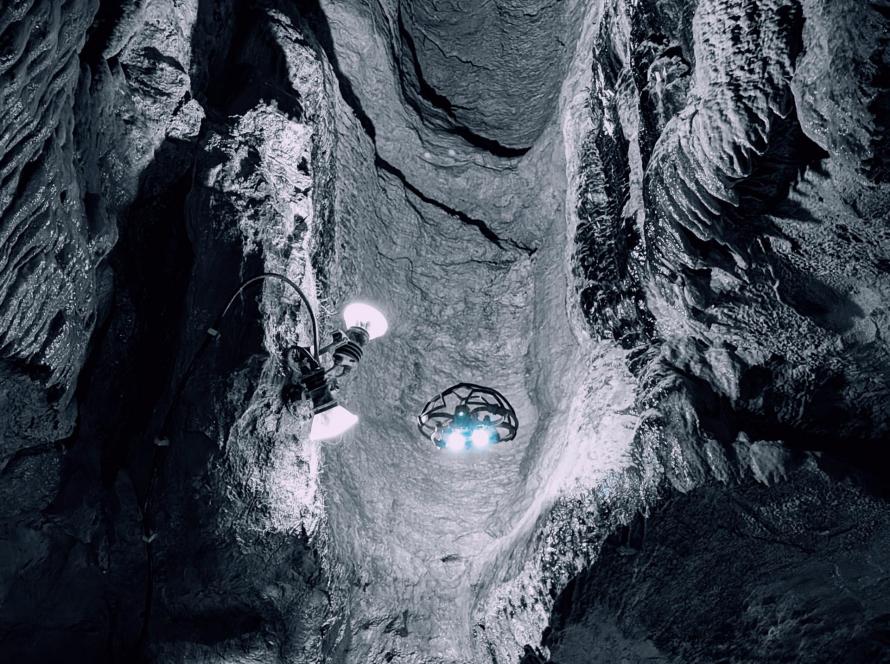 Eine hell beleuchtete Cage-Drohne steigt in einem engen, vertikalen und nassen Felsschacht auf.